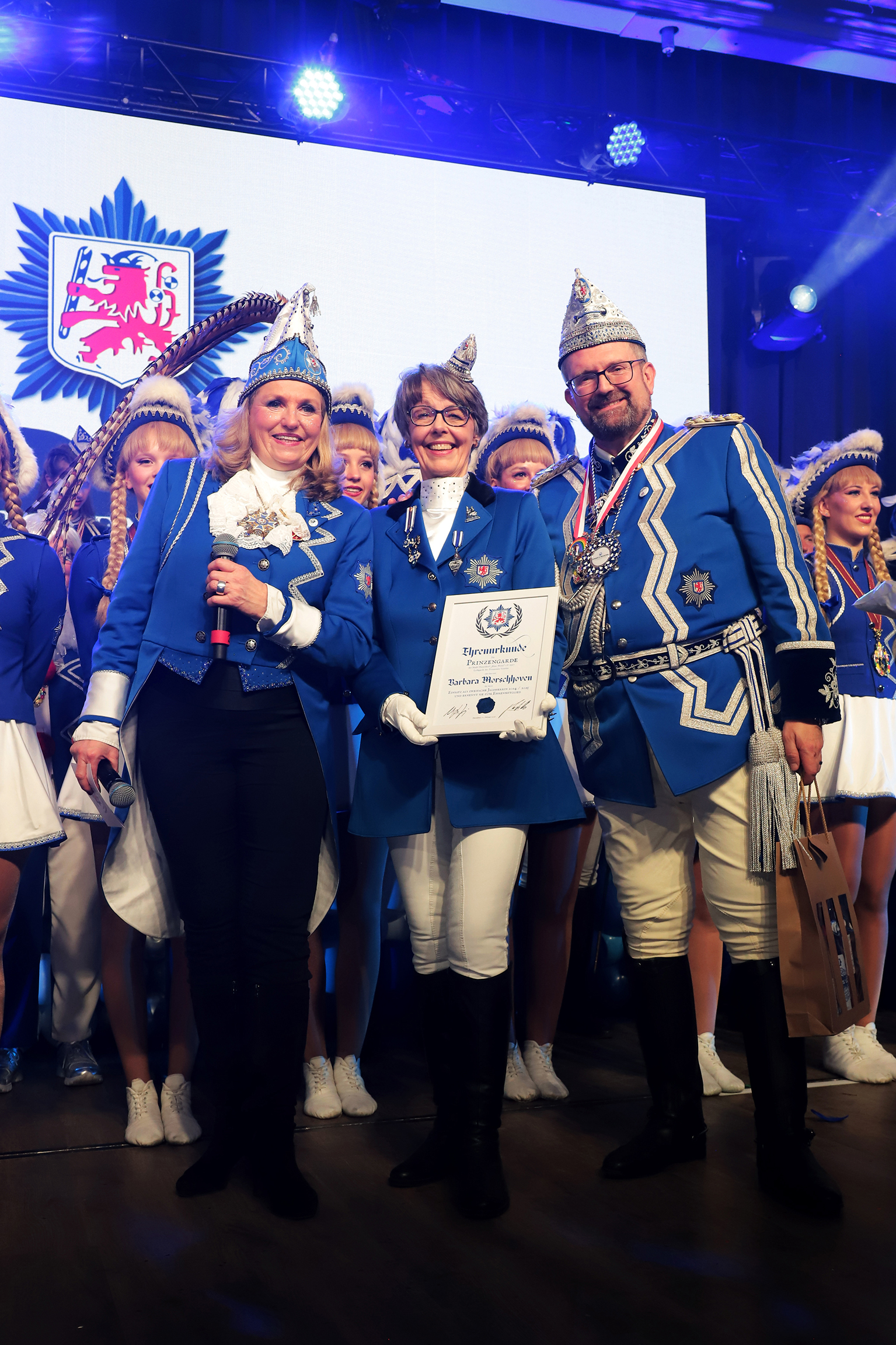 Pr&auml;sidentin Ute Heierz-Krings, Schatzmeisterin und Ehrenmitglied Barbara Morschoven sowie Vize-Pr&auml;sident Frank Minutillo auf der Jubil&auml;umssitzung vor der aufmarschierten Prinzengarde Blau-Weiss.